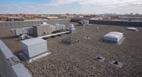 Rooftop with gravel surface, white HVAC units, and distant city skyline under a clear sky