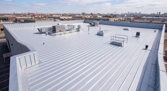 White industrial rooftop with HVAC units, vents, and distant city skyline under clear sky