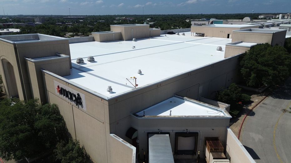 Aerial view of a beige commercial building with a white roof and surrounding trees.