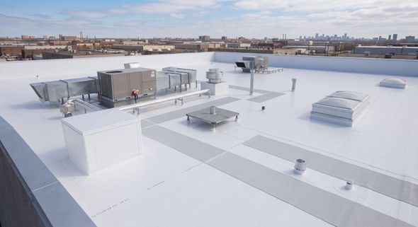 Rooftop with white flat surfaces and HVAC units, overlooking a city skyline under a clear sky