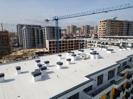 Rooftop with HVAC units overlooking apartment buildings and a construction crane in the distance