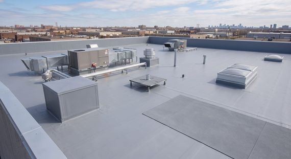 Flat commercial rooftop with HVAC units and vents under a clear sky, city skyline in the distance
