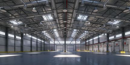 Empty industrial warehouse with high metal ceiling, large windows, and concrete floor
