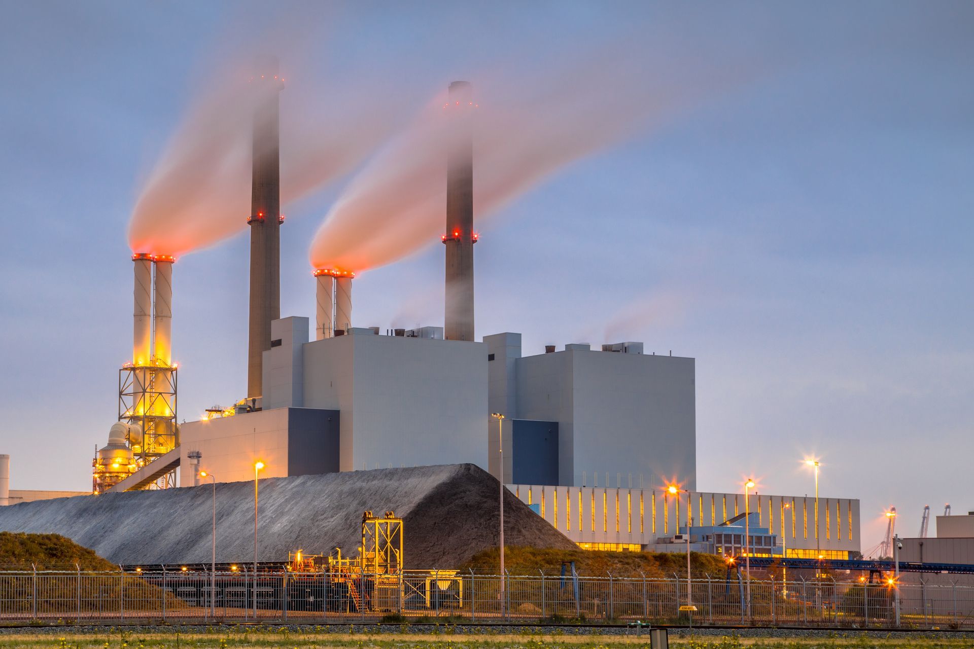 Industrial Roofing Industrial power plant with four smokestacks emitting orange-lit steam at dusk