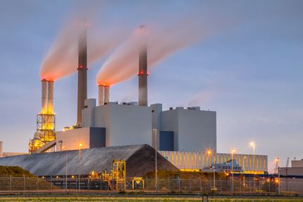 Industrial power plant with four smokestacks emitting orange-lit steam at dusk