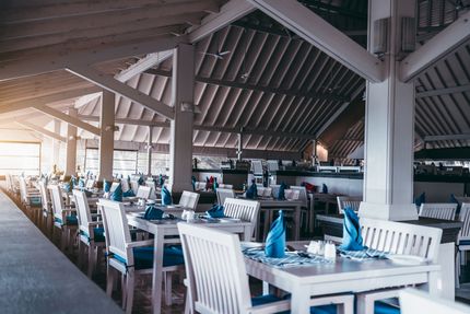 Open-air restaurant with white tables and chairs set with blue napkins under a shaded roof