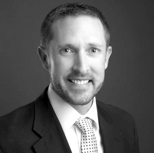 A man in a suit and tie is smiling in a black and white photo.