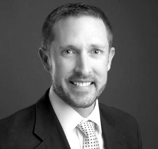 A man in a suit and tie is smiling in a black and white photo.