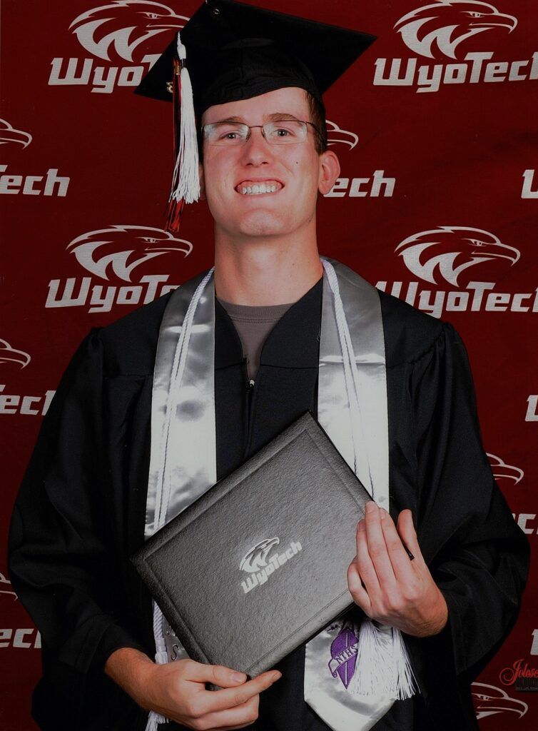 A man in a graduation cap and gown is holding a diploma