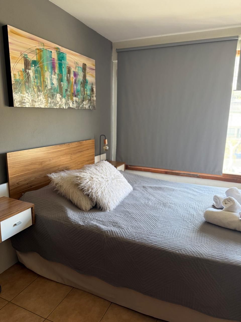 Dormitorio moderno con paredes grises, una cama, mesa auxiliar de madera, mueble para la televisión y luz de ventana.