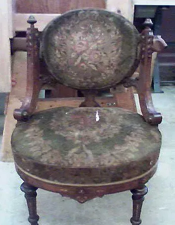 Worn antique chair with faded patterned upholstery and visible damage on the seat.