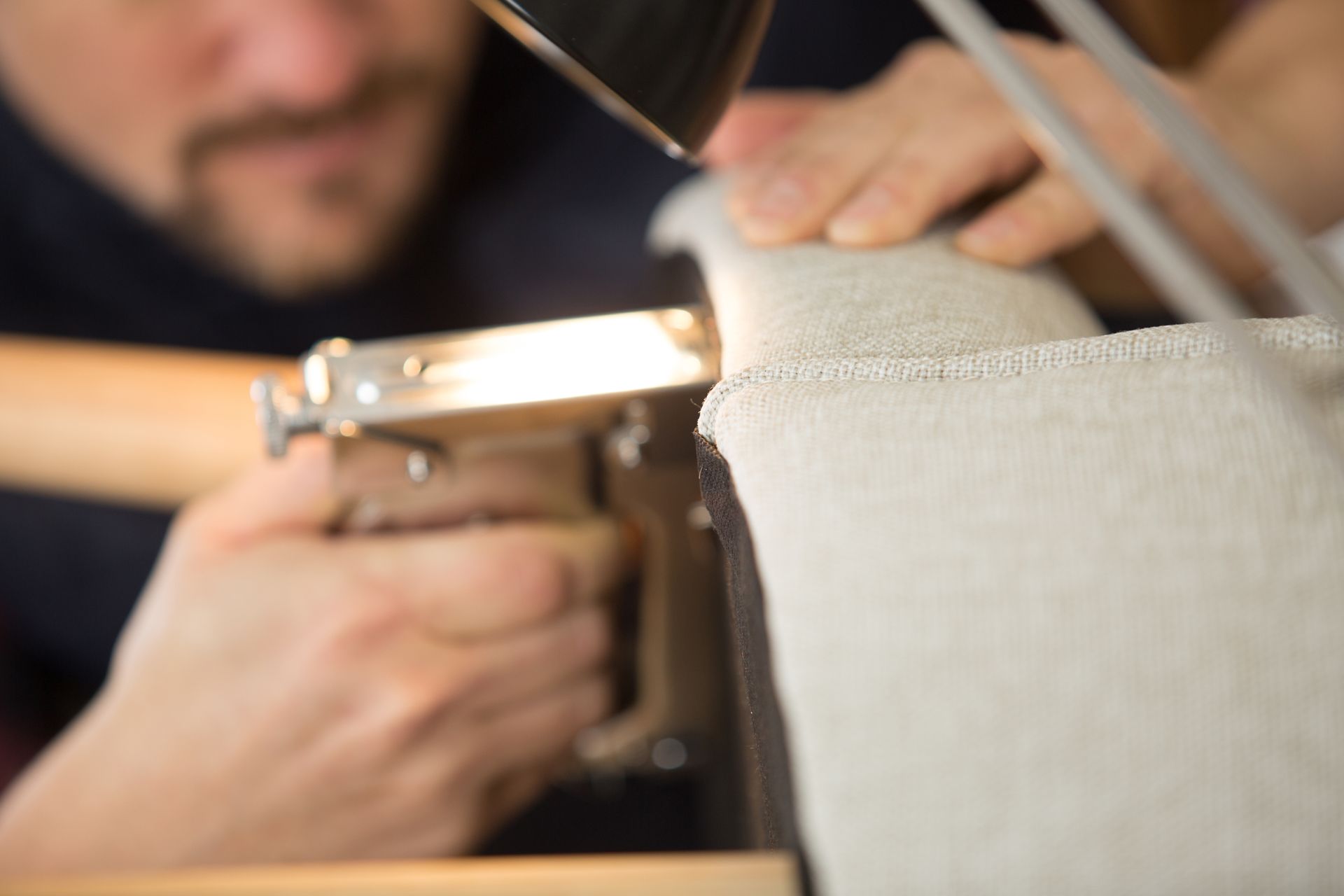 Upholstery repair specialist reupholstering a fabric sofa arm.
