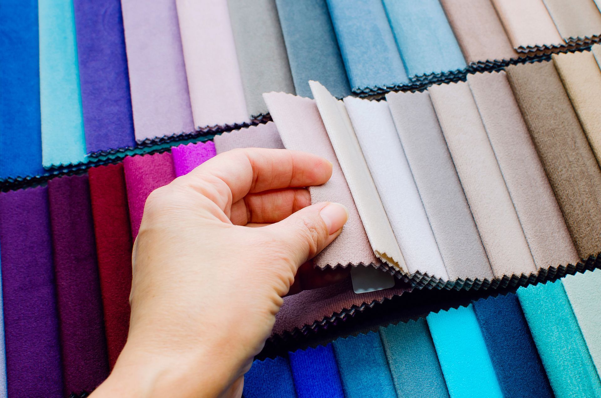 Hand selecting a fabric sample from a display of colorful upholstery swatches. Hand selecting a fabric sample from a display of colorful upholstery swatches.