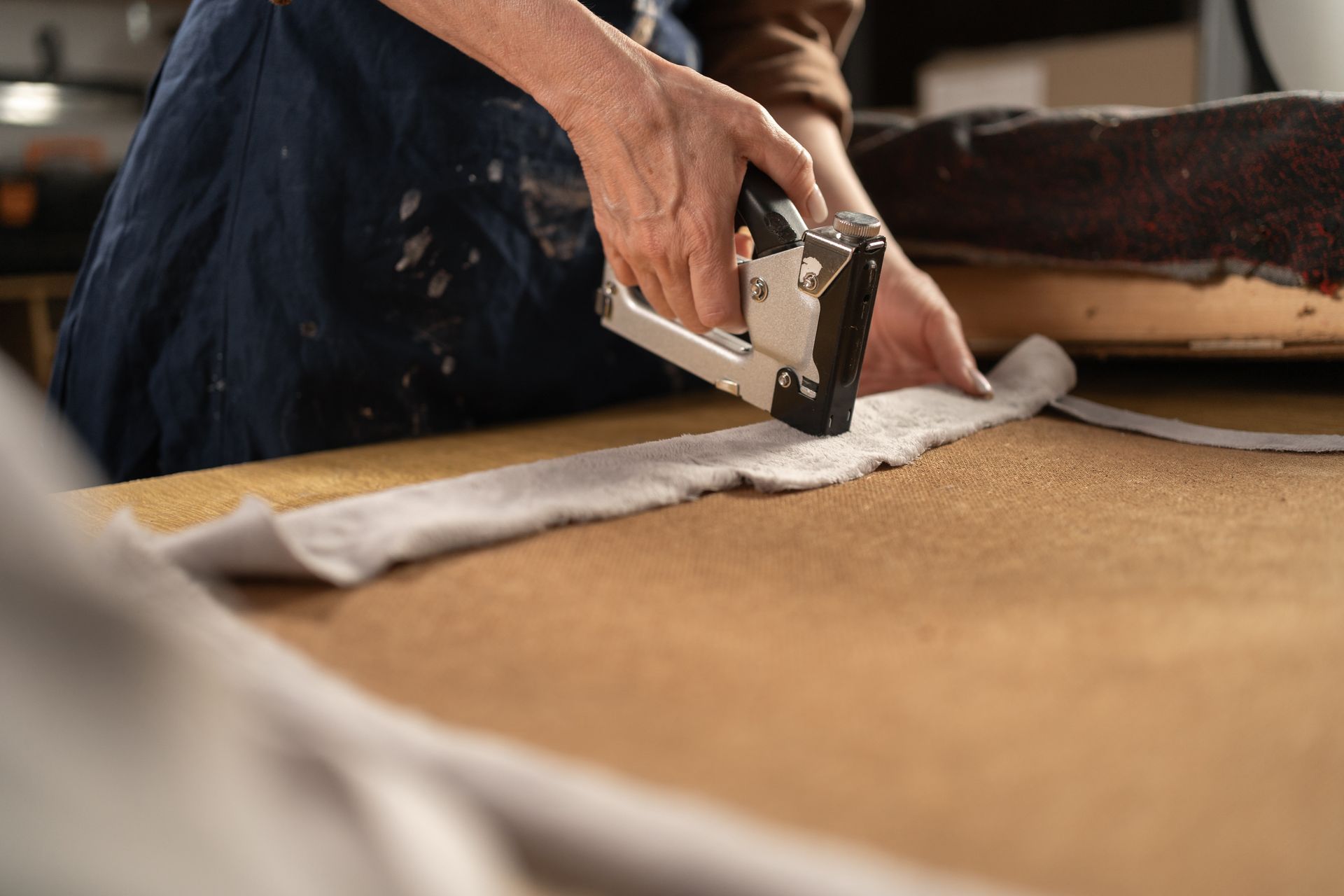 Upholsterer using a staple gun to attach fabric during professional upholstery services.