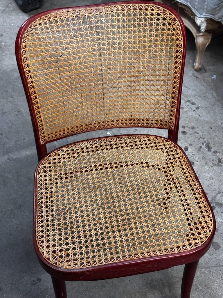 Brown cane-backed chair with a burgundy-colored frame against a gray background.