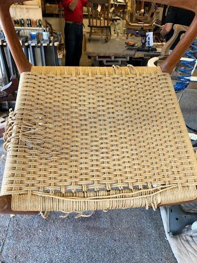 Woven chair seat with fraying fibers, in a workshop setting.