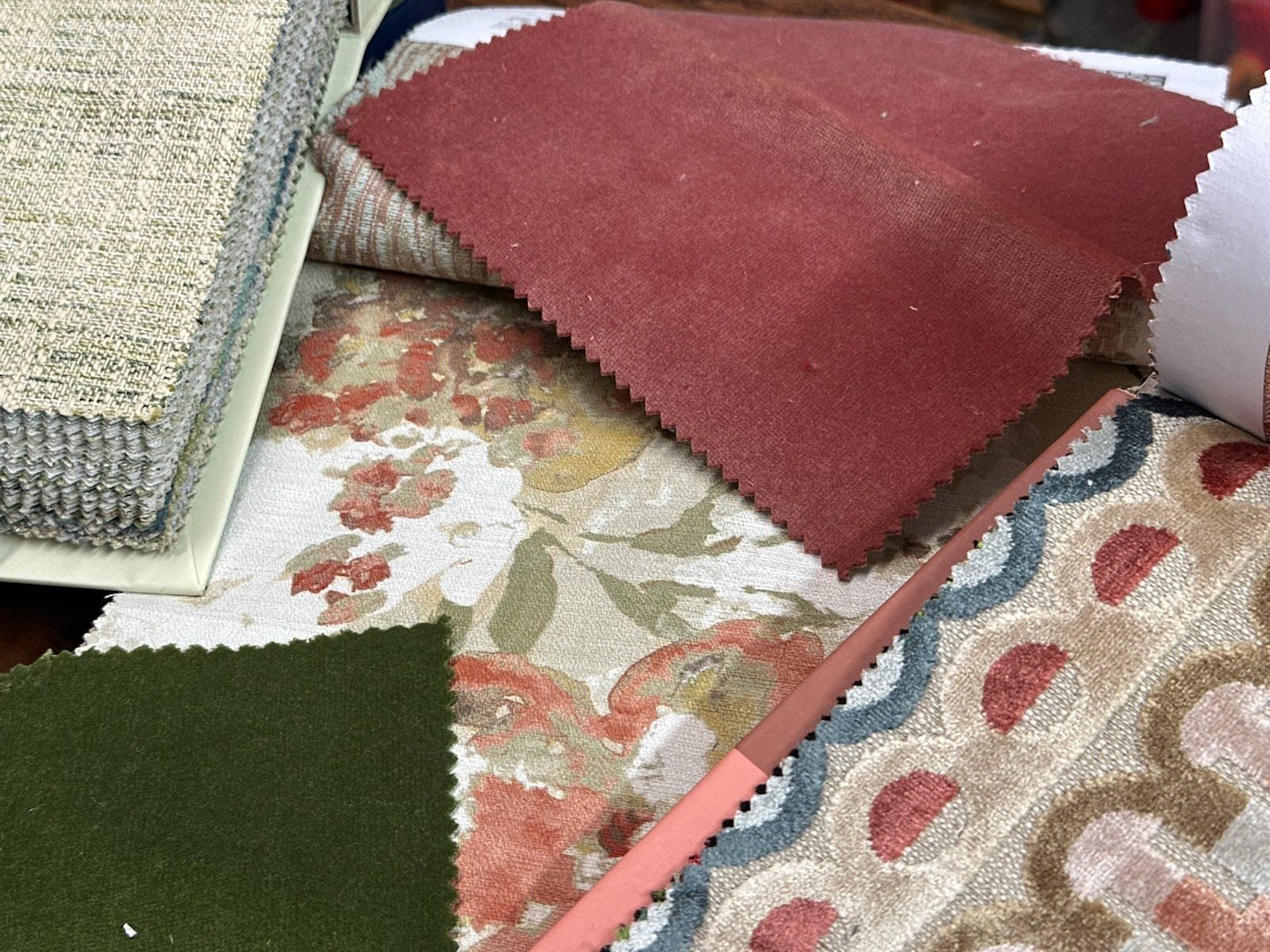 Close-up of fabric swatches in various colors and patterns, including red, green, floral, and textured neutral tones.