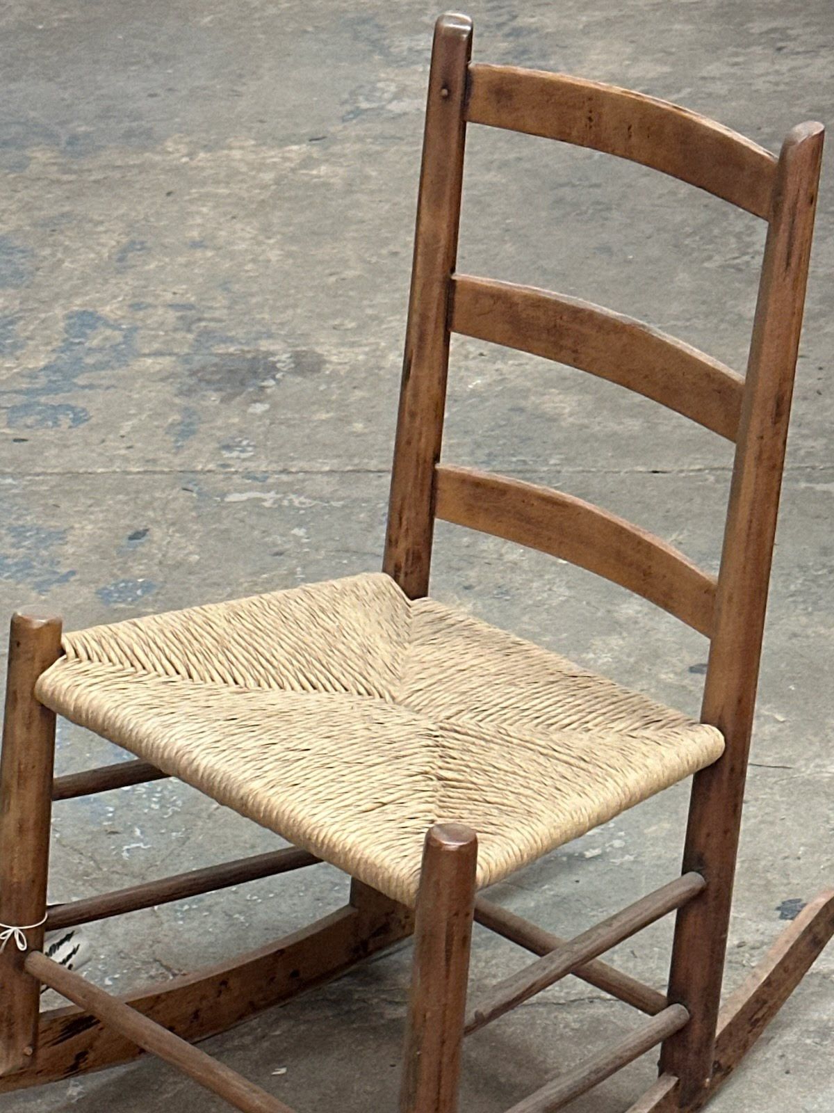 Wooden rocking chair with woven seat and back, on a concrete floor.