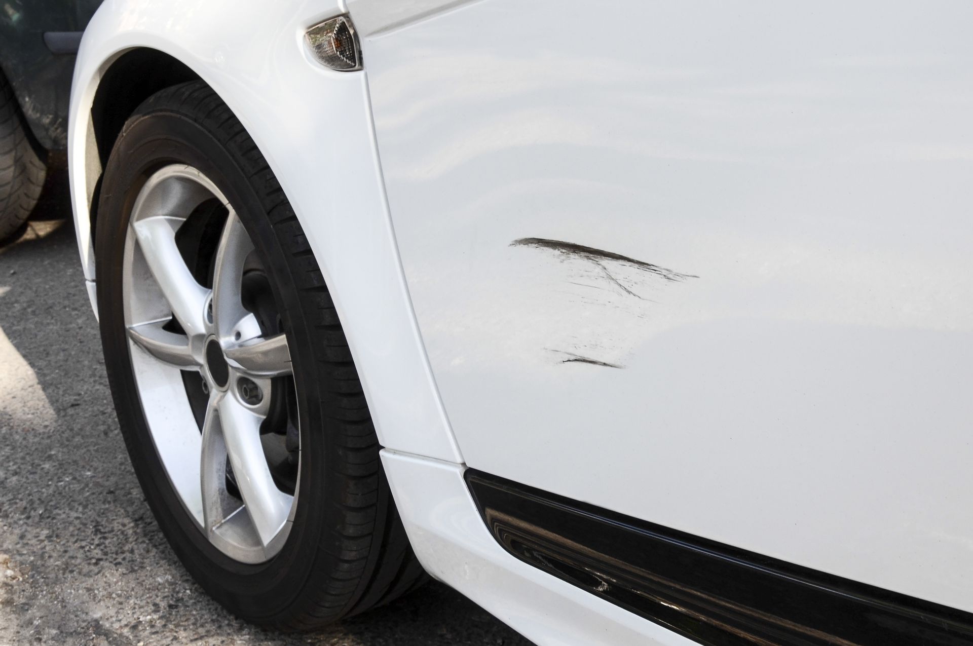 White car with a scratch on the front side panel, near the wheel.
