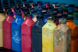 Bottles of various colorful paints lined up with black caps, indoors.
