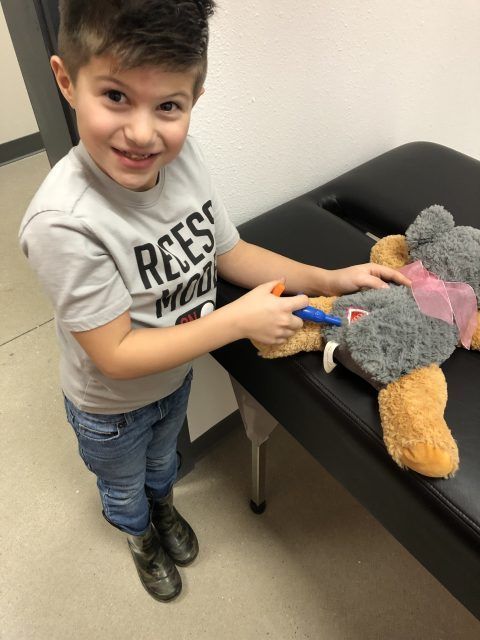 A young boy wearing a reese 's shirt is playing with a teddy bear