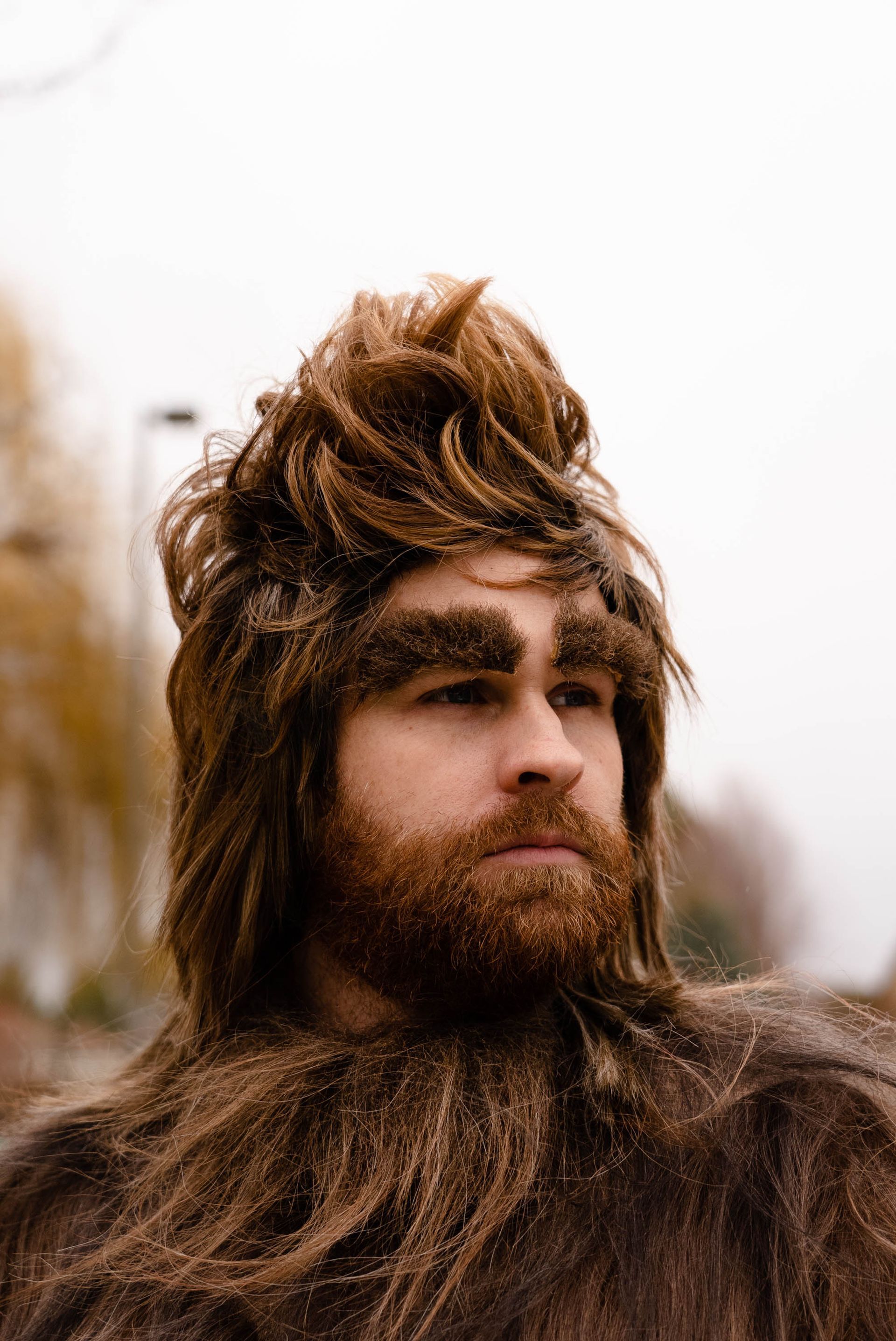 A man in a bigfoot costume is standing in front of a green background.