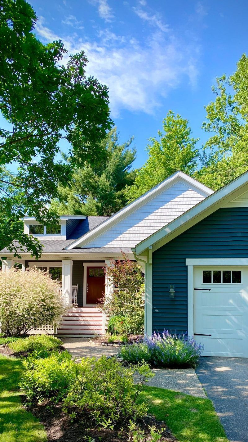 A house with a blue siding and a white garage door is surrounded by trees.
