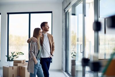 Couple looking out of a window in a new home, surrounded by moving boxes.