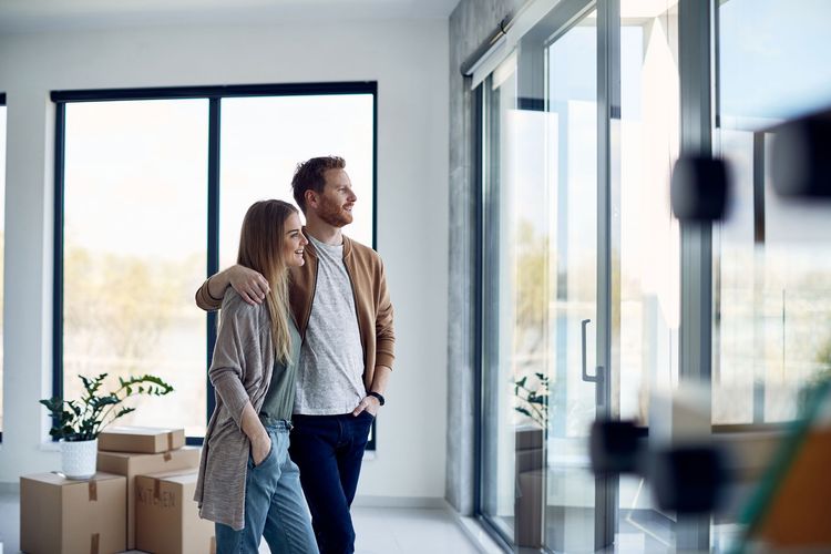 Couple looking out of a window in a new home, surrounded by moving boxes.