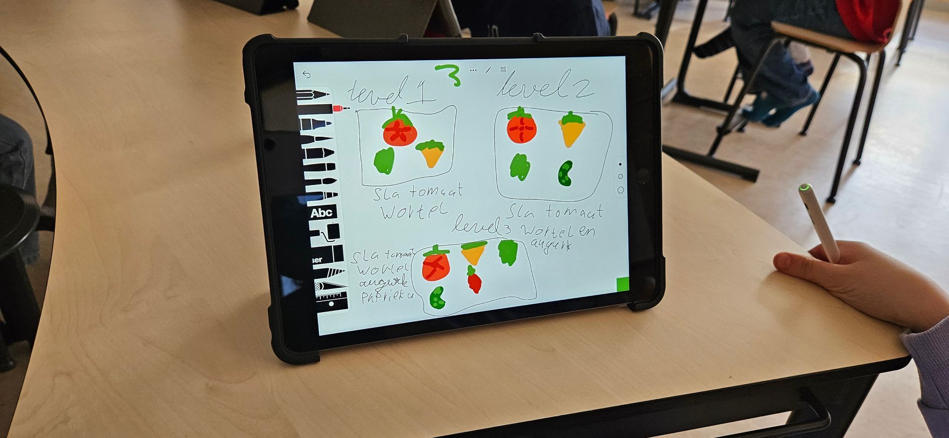 Een tablet met tekeningen van fruit ligt op een bureau. Een persoon houdt een stylus vast in zijn hand.