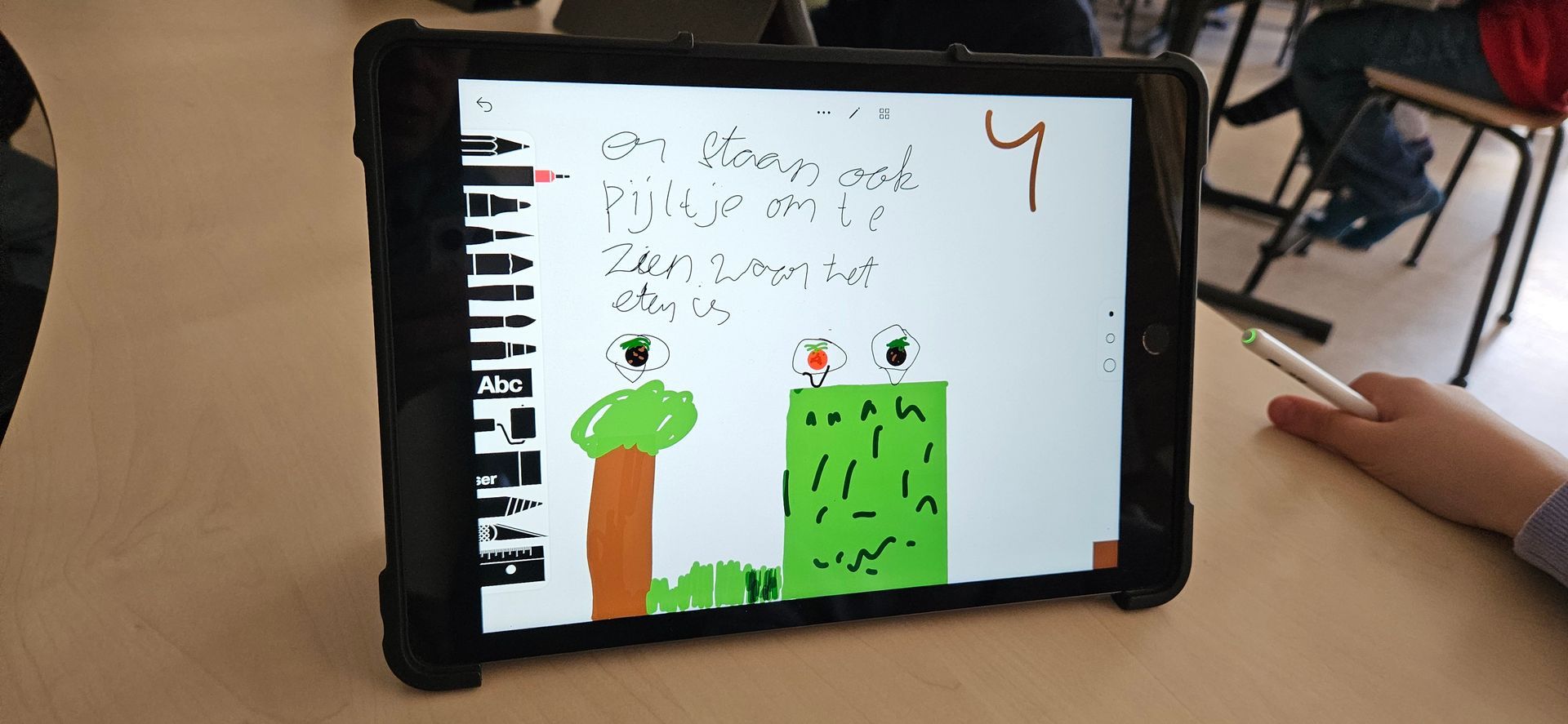Tablet waarop een kindertekening te zien is van een boom, een grasveld en het cijfer 4. Een hand houdt een stylus vast.