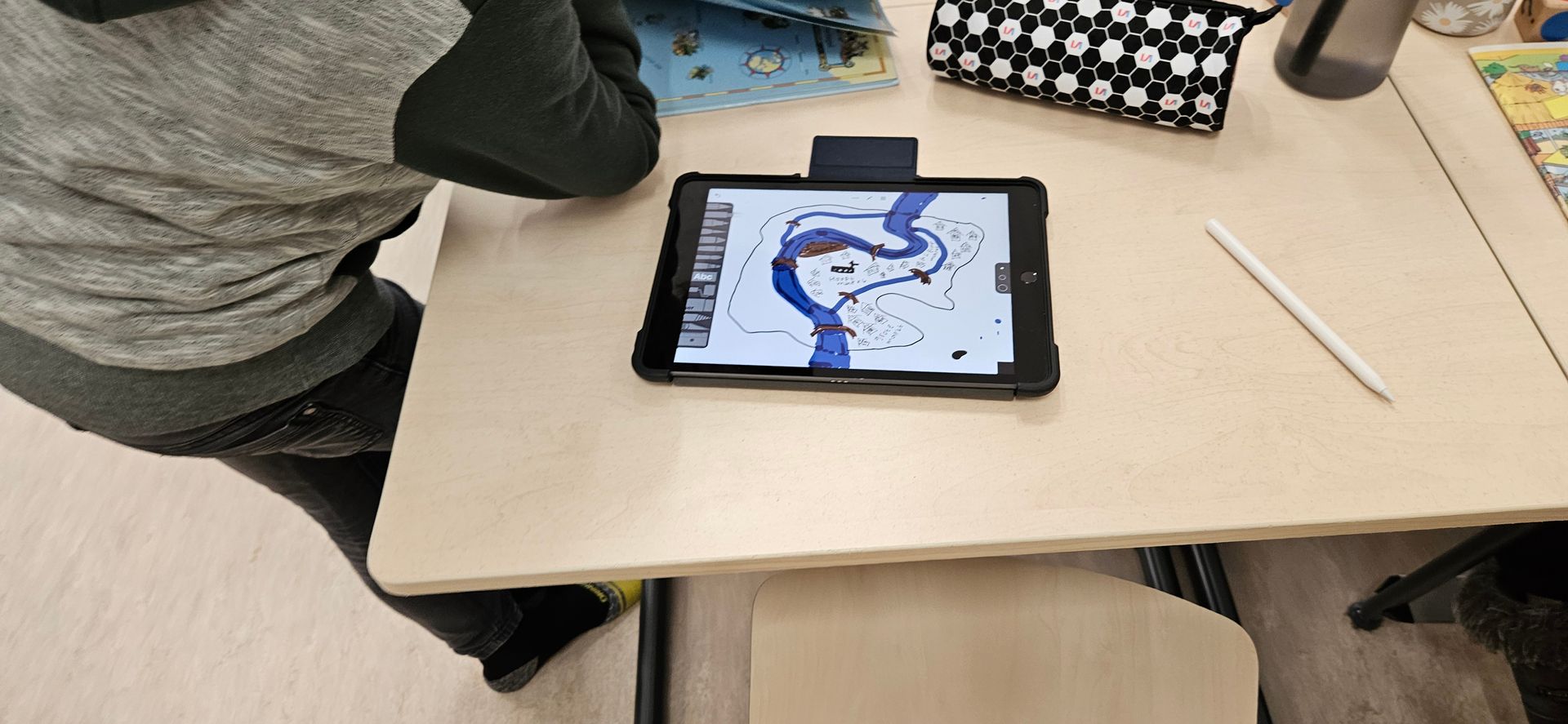Een persoon gebruikt een tablet met een stylus op een bureau. Op het scherm is een blauwe tekening te zien.