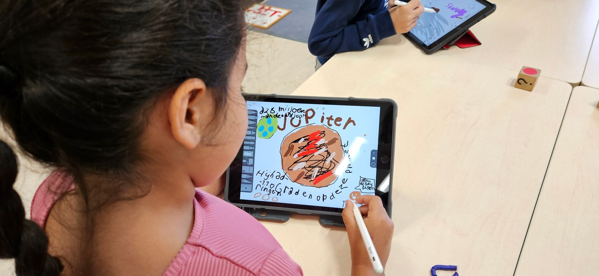 Een leerling tekent op een tablet een pizza; op de achtergrond zijn andere leerlingen en tablets te zien.