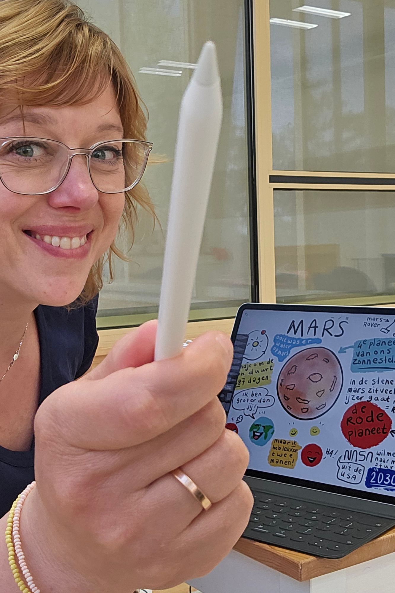 Vrouw met witte styluspen in de hand, glimlachend, met op de achtergrond een tablet waarop een