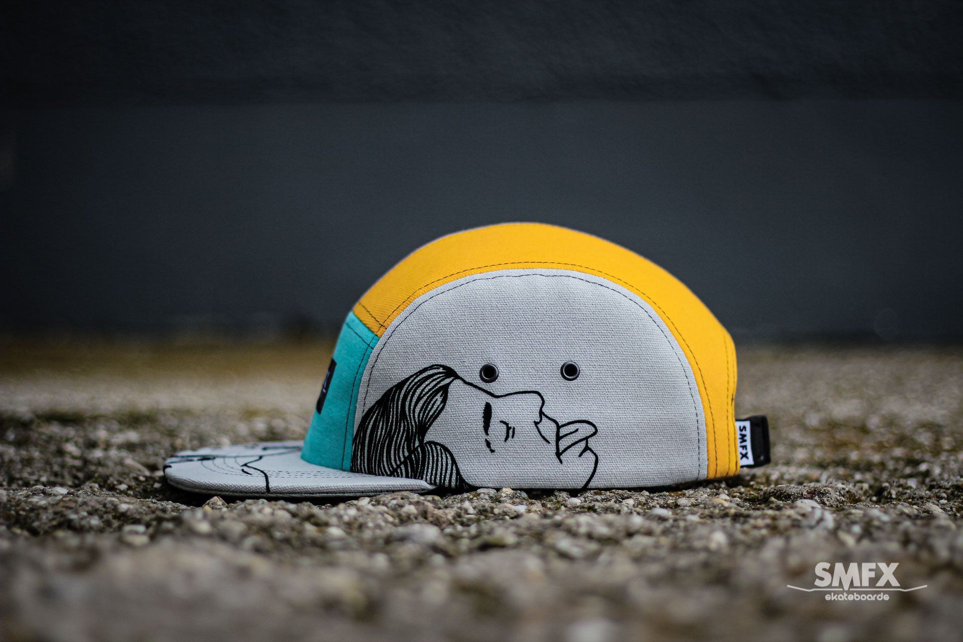 Vijfdelige pet met een gele bovenkant, grijze zijkanten en een blauw zijpaneel. De rand en het zijpaneel zijn voorzien van een zwarte lijntekening.