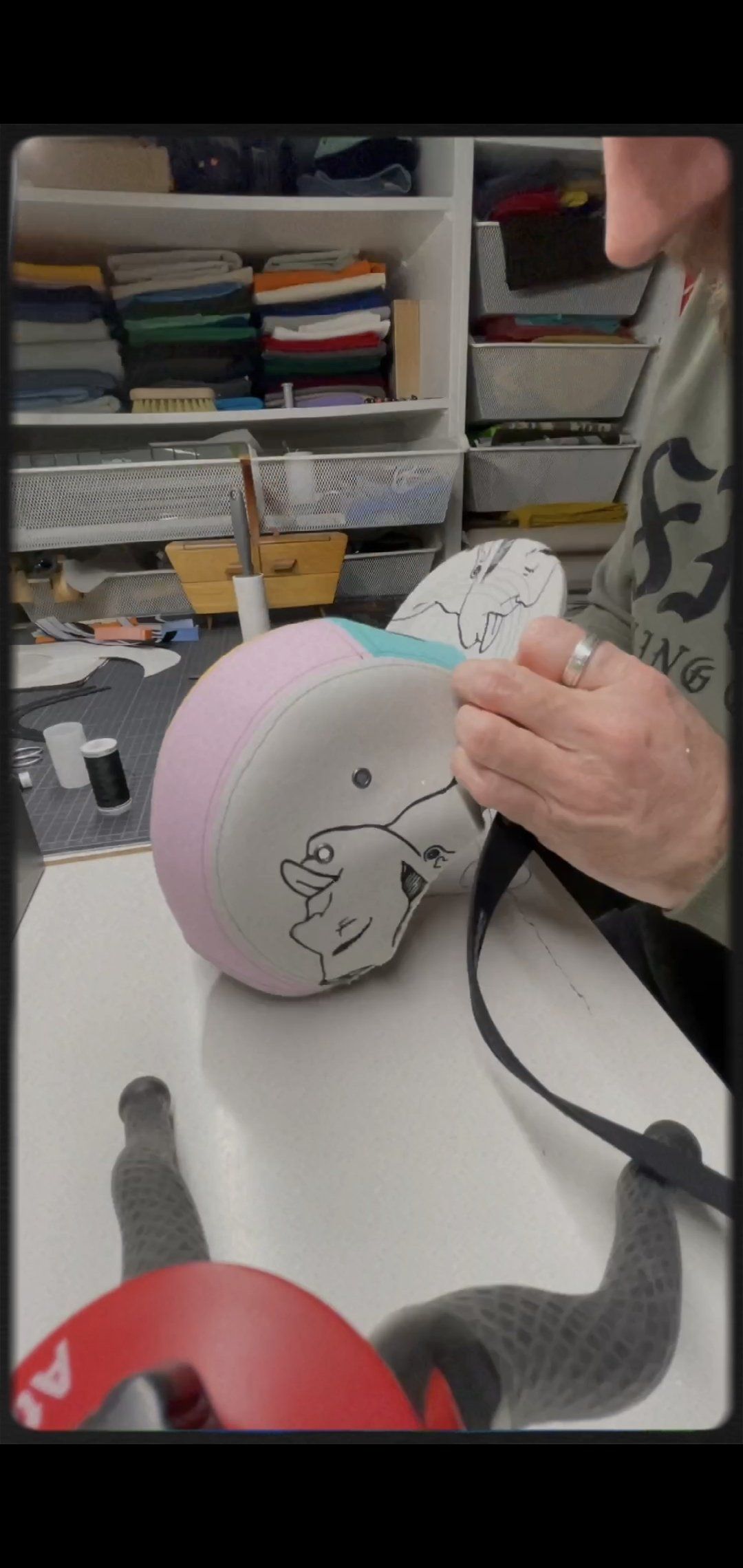 Een persoon werkt aan een roze en wit voorwerp met een zwarte band, mogelijk een helm, op een witte ondergrond.