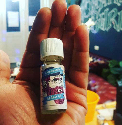 Klein flesje baardolie in een hand; etiket met een cartoonfiguur en de tekst 