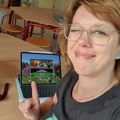 Een vrouw knipoogt en wijst naar een tablet waarop Minecraft wordt weergegeven in een klaslokaal.
