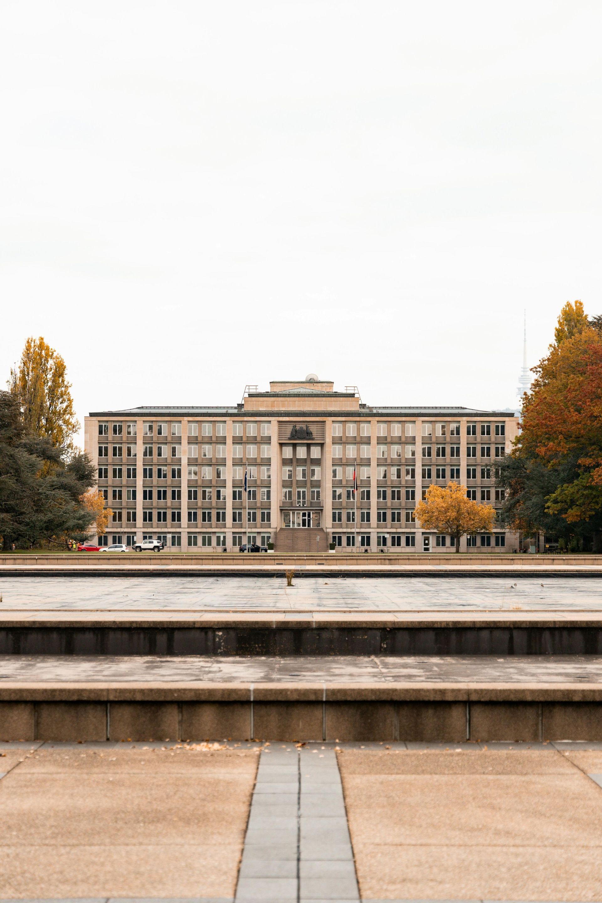 Wide stone steps leading to a modern building framed by autumn trees under a cloudy sky