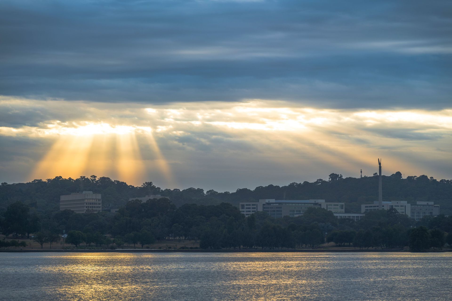 Sunbeams breaking through clouds over a waterfront city skyline at dusk