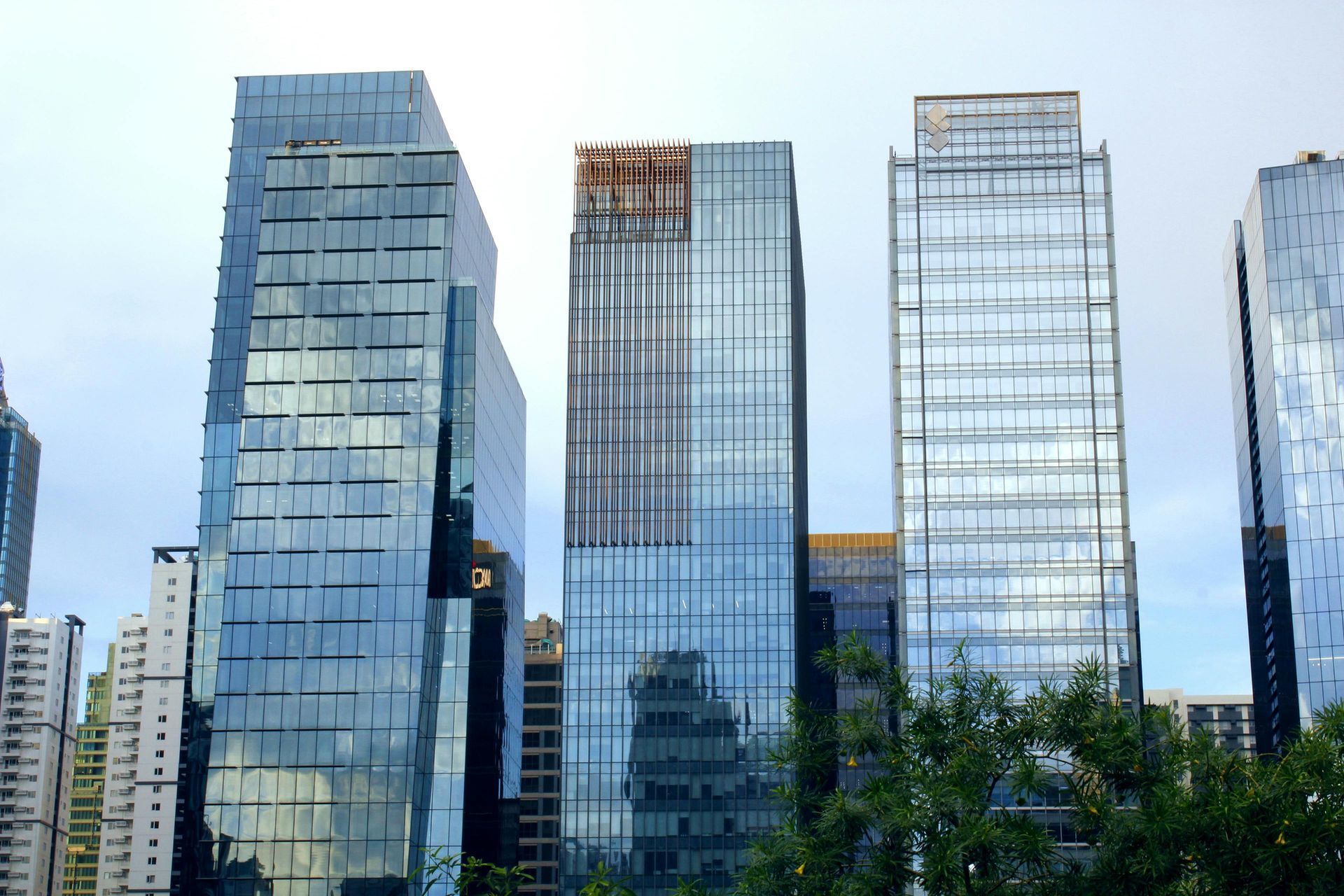 Modern glass office towers against a cloudy sky with trees in the foreground