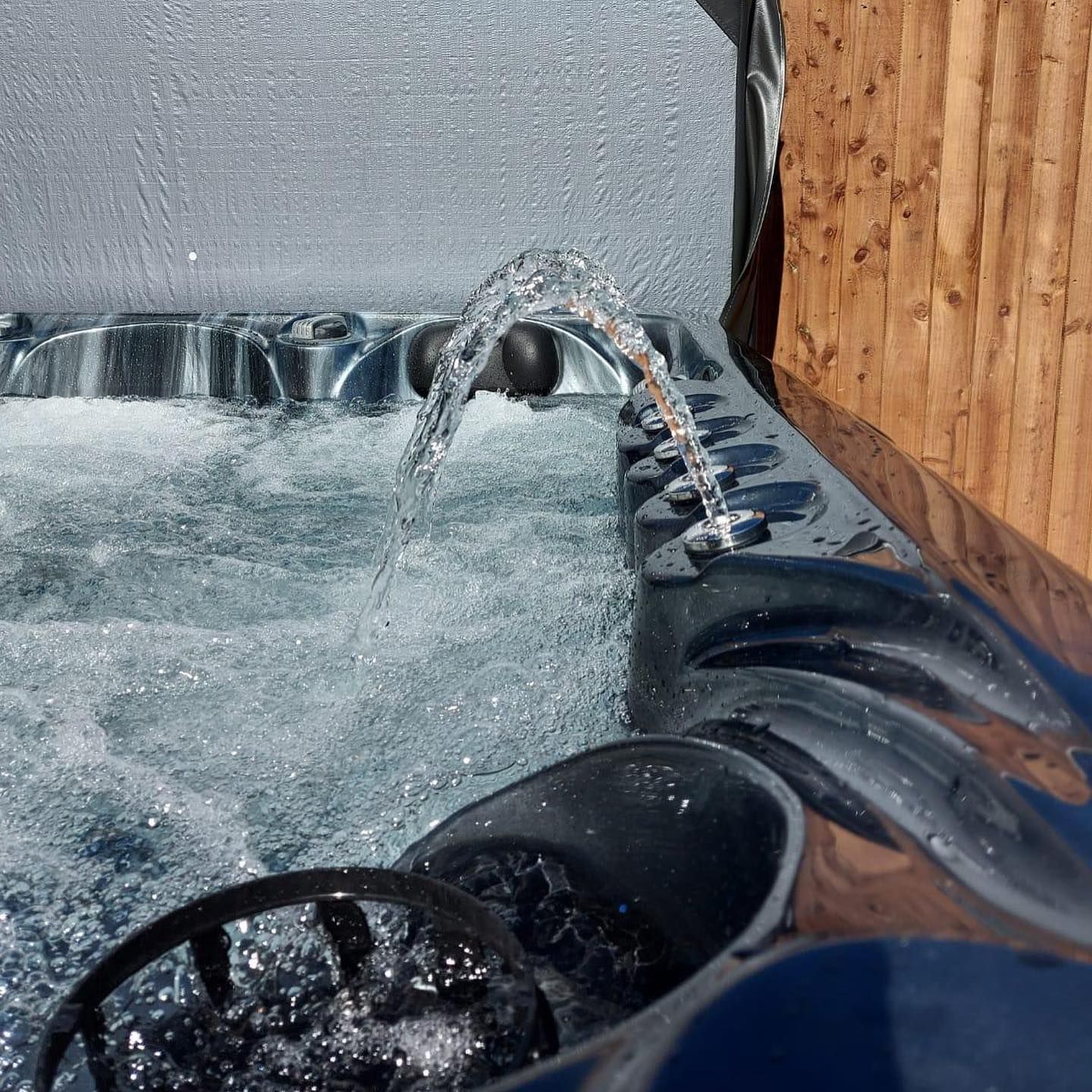 Hot tub with bubbling water and a water fountain against a wooden fence.