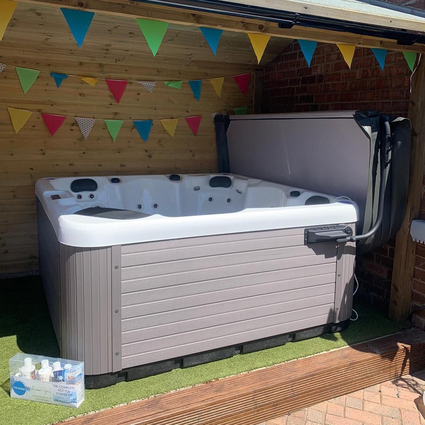 Hot tub with open cover under a wooden shelter, decorated with colorful bunting.