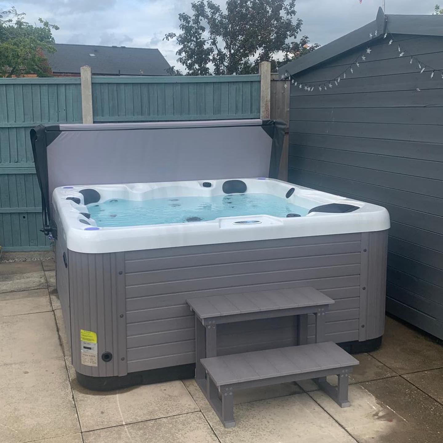 Gray hot tub with partially open cover, on a patio, with steps.