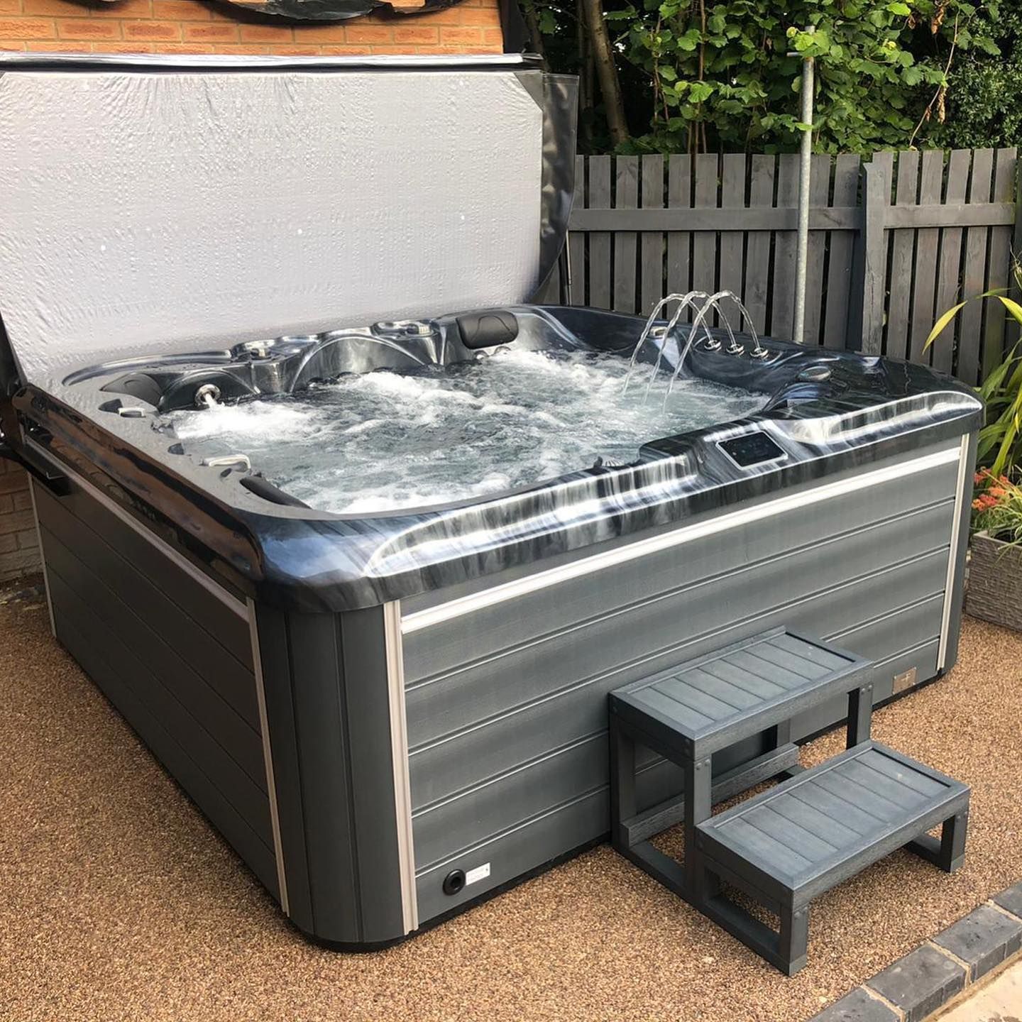 Gray hot tub with bubbling water, partially covered, next to a two-step stool in an outdoor setting.