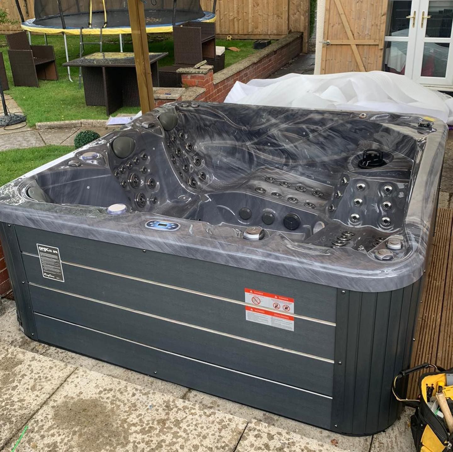Dark gray hot tub on patio, with jets and control panel visible. Backyard setting.