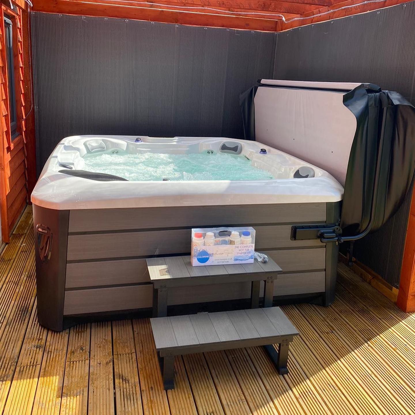 Hot tub with cover open, on a wooden deck in a covered structure. Steps in front.
