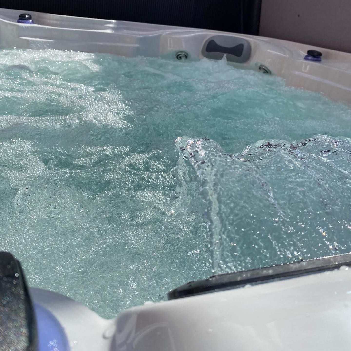 Bubbling hot tub with jets creating water movement. Blue-tinted water within a white tub.