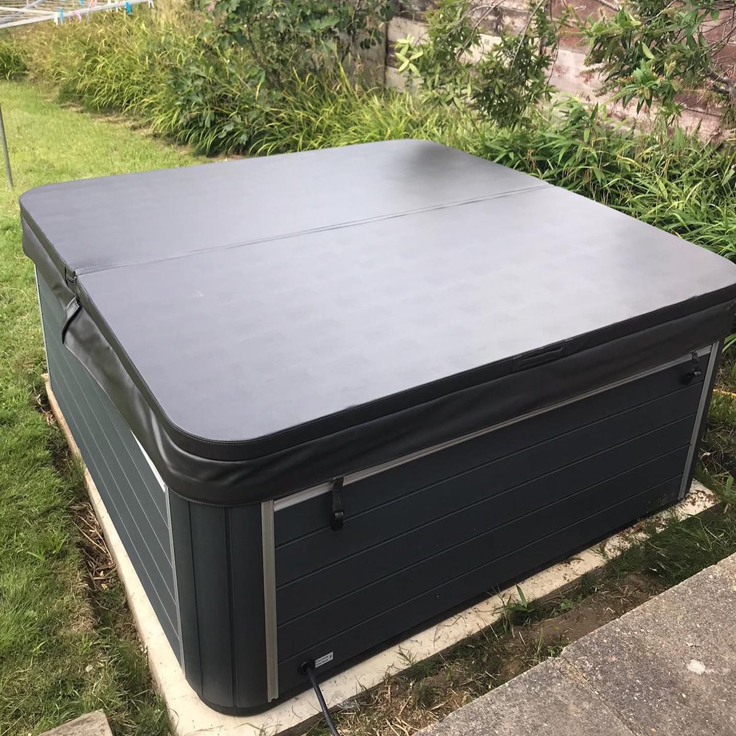 Dark hot tub with a closed cover, set in a grassy yard.