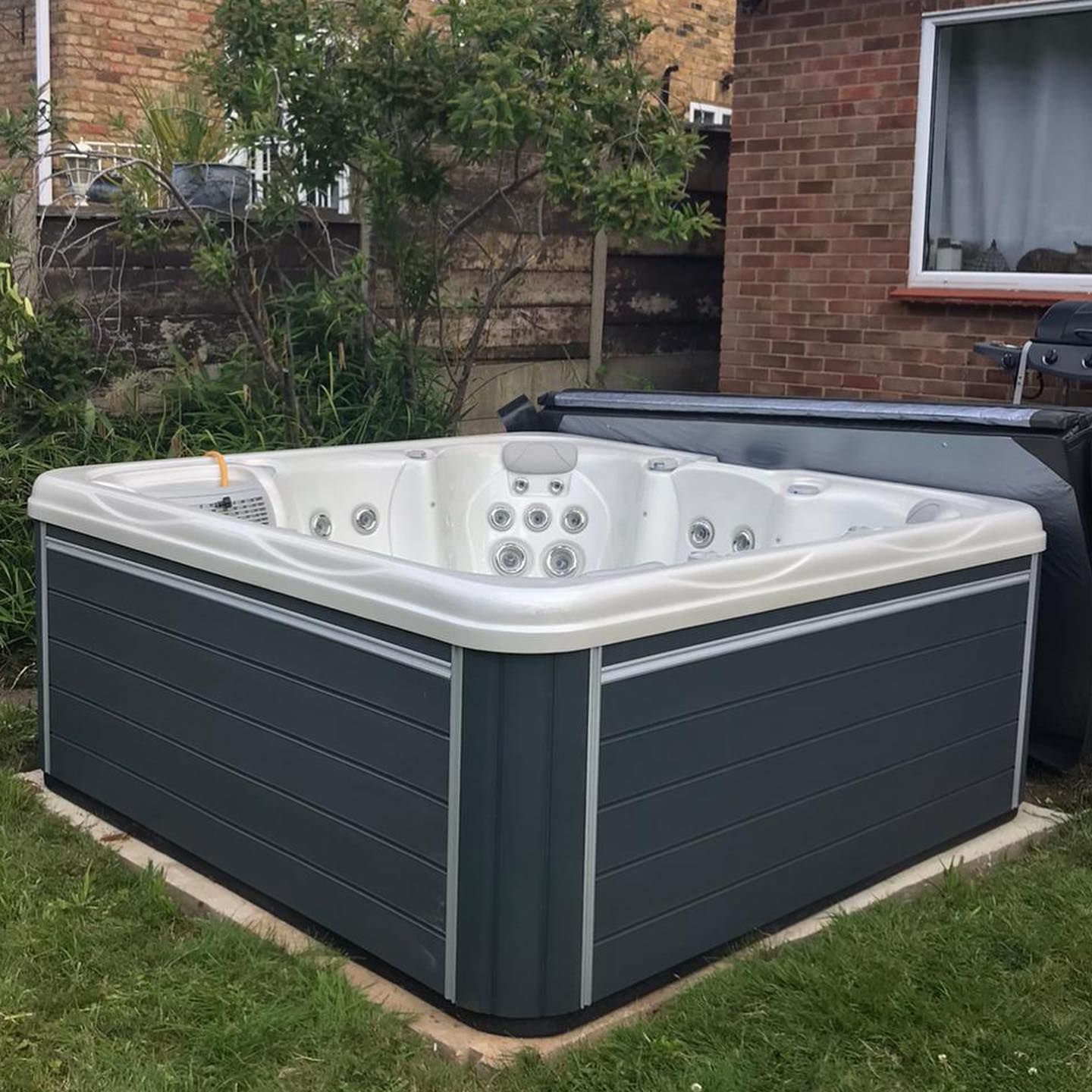 Gray hot tub in a backyard with a brick building and green grass.